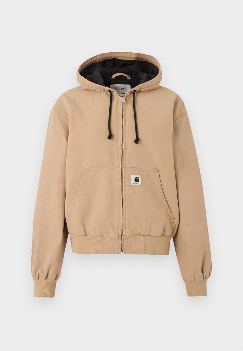Veste à capuche beige zippée avec cordons noirs, poches kangourou à l’avant, poignets côtelés et écusson avec le logo Carhartt sur la poche avant.