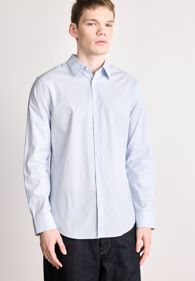 Camisa azul claro con rayas blancas, de botones, mangas largas, cuello estándar y dobladillo curvo. El material parece suave y sutil.