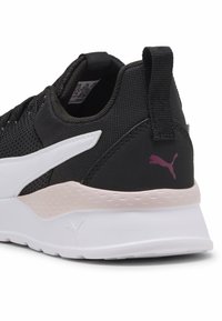 Baskets de sport noires avec un dessus en mesh, des accents blancs et une semelle texturée rose et blanche avec un logo Puma à l'arrière.