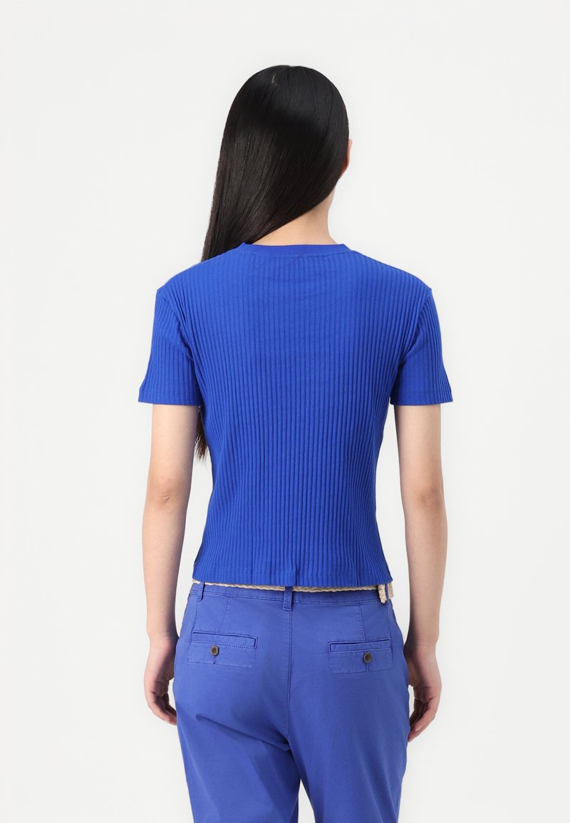 Niebieski, prążkowany top z krótkim rękawem, okrągłym dekoltem i dopasowanym krojem z teksturowanej tkaniny. Noszony z dopasowanymi, niebieskimi spodniami z tylnymi kieszeniami.