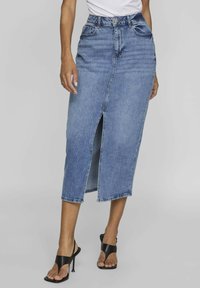 Denim midi skirt with a front slit, light blue wash, high waist, five pockets, and belt loops, paired with black heeled sandals.
