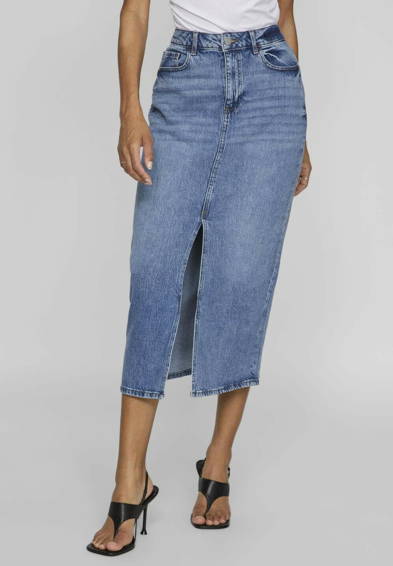 Denim midi skirt with a front slit, light blue wash, high waist, five pockets, and belt loops, paired with black heeled sandals.