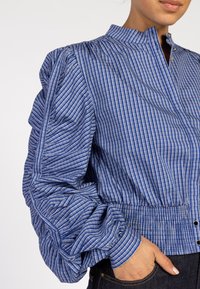 Blauw-wit gestreepte blouse met pofmouwen en een mandarinakraag, voorzien van een rits en een geraffineerde taille. Gemaakt van katoen.