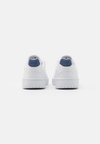 Weiße Turnschuhe aus glattem Leder, mit einem blauen Akzent an der Ferse und einer strukturierten Gummisohle. Minimalistisches Design.