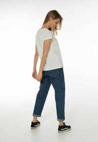 Witte korte mouwen top gecombineerd met blauwe spijkerbroek, met een relaxte pasvorm en opgerolde mouwen, gedragen met zwart-witte sneakers.