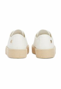 Weiße Leinenschlupfschuhe mit einer strukturierten beige Seilsohle und einem kleinen goldfarbenen Logoakzent an der Ferse.