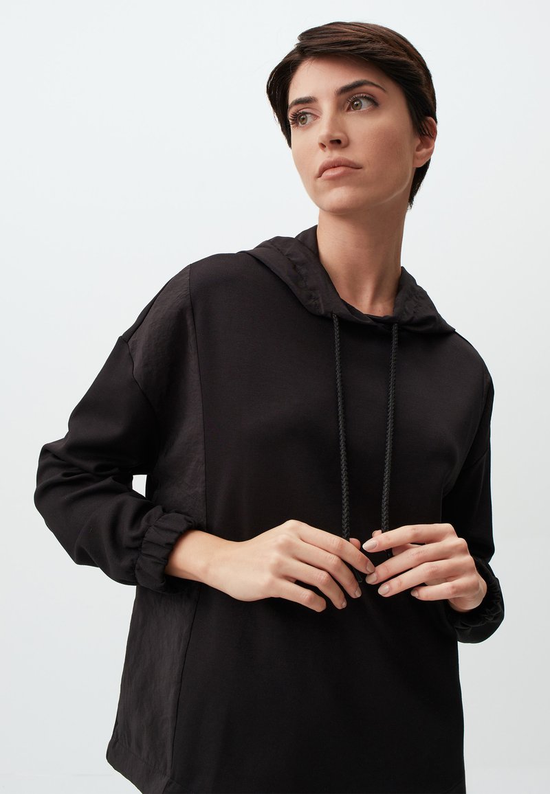 Sweatshirt à capuche noir à manches longues, présentant un tissu texturé sur la partie supérieure, des accents de cordons de serrage et des poignets élastiques.