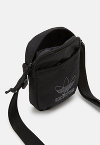 Černá nylonová krosbody taška se zipovým uzávěrem, přední kapsou a bílým logem Adidas. Nastavitelný popruh pro pohodlí.