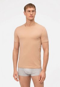Beige T-shirt met korte mouwen gemaakt van gladde stof, voorzien van een ronde hals en minimalistisch ontwerp, gedragen met grijze boxershorts.