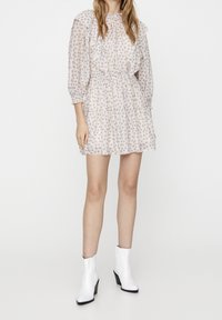 Robe courte à imprimé floral avec col et manches à volants, taille élastique et jupe à volants ; tissu léger dans des couleurs pastel douces.