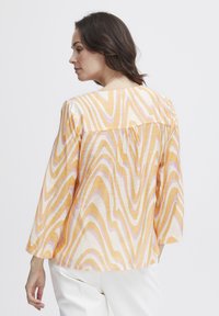Langærmet bluse med et bølget mønster i gul, orange og pink; knapper på ryggen; let, tekstureret stof.