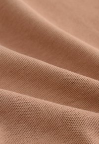 Tissu tricoté brun clair avec une texture lisse, présentant des tissages subtils et serrés ainsi que des plis doux créant profondeur et dimension.