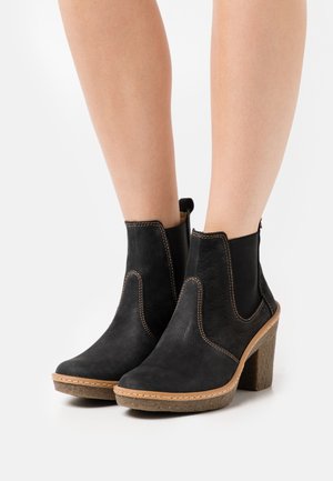 Bottines noires avec une finition en cuir lisse, des panneaux latéraux élastiques et un talon en liège texturé, présentant des détails de couture contrastants.