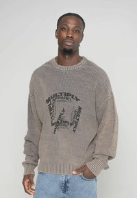 Übergrößiger, hellbrauner Pullover mit gerippter Textur. Mit schwarzem Grafiktext "MULTIPLY APPAREL". Gerippte Bündchen und Saum, lässige Passform.