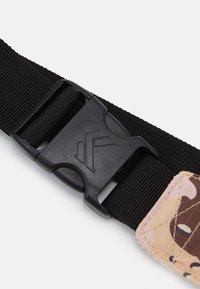 Černý nylonový pásek s plastovou sponou a logem. Jeden konec má látku v růžovém a hnědém maskáči, ozdobenou prošitím.