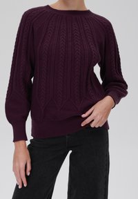 Lila gestrickter Pullover mit geripptem Struktur, der vertikale Muster und einen Rundhalsausschnitt bietet. Lange Ärmel und eng anliegende Bündchen runden das Design ab.