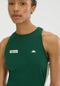 Groene mouwloze sporttop in een gladde stof, met een wit logo-label en accent bij de halslijn en details met zijstrepen.