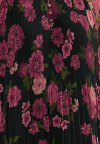 Mustalla kankaasta valmistettu mekko, jossa on pystysuuntaiset poimutukset, ja joka on koristeltu suurilla vaaleanpunaisilla ja purppuranvärisillä kukkamalleilla sekä etuosassa napit.