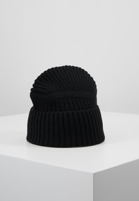 Mustat neulottu pipo, jossa on pystysuora ribbaus ja pyöreä yläosa, valmistettu pehmeästä materiaalista. Pohjassa on taitto.