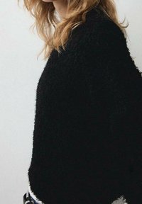 Pull noir duveteux à coupe décontractée. Texture douce et encolure arrondie, avec un ourlet irrégulier. Design minimaliste et tissu léger.