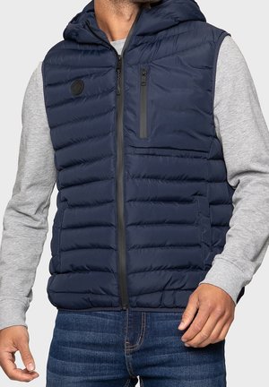 Marineblauw puffer vest met capuchon, voorzien van een ritssluiting aan de voorkant, twee zijzakken en een ritszak op de borst; zachte textuur en gewatteerd patroon.