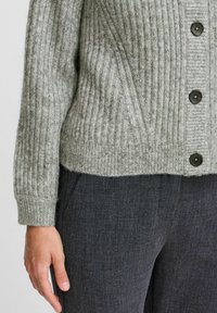 Cardigan grigio a coste realizzato in morbido materiale knit, caratterizzato da un collo alto, una vestibilità oversized e bottoni scuri lungo la parte anteriore.