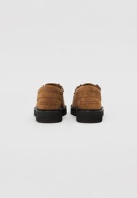 Chaussures en daim marron avec une texture lisse, bout rond et semelles en caoutchouc noir. Présentent des coutures horizontales et des éléments décoratifs sur le côté.