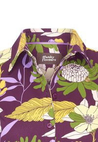Camicia viola con motivo floreale in giallo, verde e bianco. Presenta un colletto a risvolto, bottoni viola e un'etichetta con la scritta "4funky flavours."