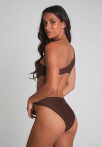 Brun enaxlad bikini, sömlös design, slät textur. Höga trosor med sidodetaljer, minimal täckning och åtsittande stil.