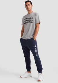 Gray t-shirt with black "O'NEILL" logo, paired with navy joggers featuring white "O'NEILL" text. White athletic shoes complete the look.