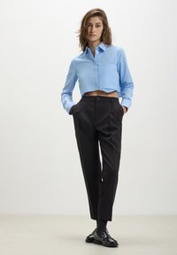 Camicetta blu corta con bottoni e una tasca abbinata a pantaloni neri a vita alta e mocassini neri lucidi.