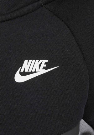 Musta Nike-huppari, jonka kangas on sileä. Korostaa suurta valkoista Nike-logoa ja tyylikästä ommelta hartioiden kohdalla.