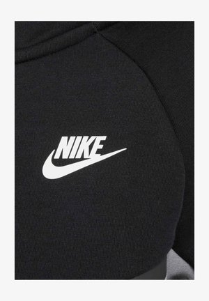 Musta Nike-huppari, jonka kangas on sileä. Korostaa suurta valkoista Nike-logoa ja tyylikästä ommelta hartioiden kohdalla.