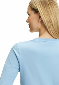 Helles blaues Langarmshirt mit rundem Halsausschnitt, aus weichem, glattem Stoff gefertigt. Verfügt über ein einfaches Design ohne Muster oder Akzente.