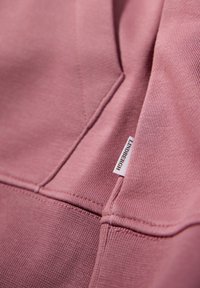 Tela de algodón rosa con una textura suave, que presenta detalles de costura y una pequeña etiqueta blanca con "LANDERBERGH" en el borde.