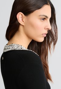 Pullover nero con colletto di perline decorate con strass trasparenti. Il design include una texture a coste lungo le spalle.