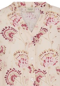 Blouse beige clair avec un col montant et un motif floral rose, rouge et beige, fermeture à boutons sur le devant, et étiquette "fransa" au niveau du col.