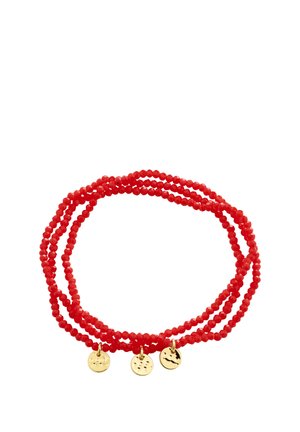 Czerwona bransoletka z koralików z trzema małymi okrągłymi złotymi zawieszkami rozmieszczonymi równomiernie, pokazana zwinięta na białym tle.
