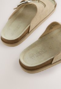 Sandales ouvertes beige en daim avec semelle intérieure en liège, brides réglables à boucle et semelles en caoutchouc texturées sur une surface claire.