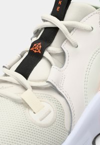 Hvid sportsko med en mesh-overdel, teksturerede paneler, sorte og orange snørebåndsdetaljer og et polstret således design.