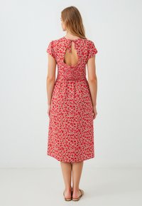 Rode bloemenjurk met korte mouwen, een smocktail en een keyholeopening op de rug. Zacht materiaal met kleine witte bloemenpatronen erdoorheen.