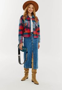 Pestrý károvaný blejzer s dvoma náprsními vreckami, skombinovaný s modrou riflovou sukňou s predným rozparkom a gombíkovým uzáverom, a hnedými čižmami.