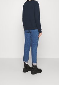 Marinblå sweatshirt med rund halsringning, blåjeans som är uppvikta vid bensluten, och svarta ankelboots med robust sula. Enkel, avslappnad stil.