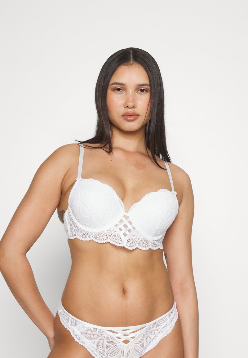 Ensemble de lingerie blanc en dentelle, comprenant un soutien-gorge et une culotte assortie, avec un bord festonné, des motifs intriqués et des bretelles réglables avec des détails croisillons.