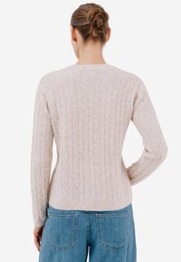 Beżowy sweter w warkoczowy splot z długimi rękawami i okrągłym dekoltem. Miękka, teksturowana tkanina o dopasowanym kroju. Połączony z niebieskimi dżinsami.