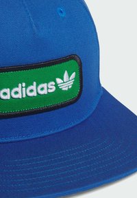 Blaues Cap aus Stoff mit flachem Schirm. Auf dem Schild befindet sich ein grünes gesticktes Patch mit "adidas" in weißem Text und Logo. Schwarzer Rand um das Patch.