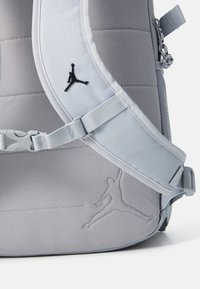 Gray backpack with textured fabric. Features a black logo and adjustable straps. Includes buckle hardware and embossed design details.