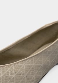 Μπεζ επίπεδο παπούτσι με υφαντό σχέδιο διαμαντιού και σχήματα ημισελήνου, που δείχνει ομαλή εσωτερική επένδυση και στρογγυλεμένη πάνω άκρη.