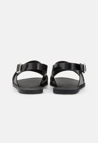 Μαύρες σανδάλια με ρυθμιζόμενους ιμάντες για τον αστράγαλο, κατασκευασμένα από λεία δέρμα και υλικό με υφή. Διαθέτουν επίπεδη σόλα και μινιμαλιστικό σχέδιο.