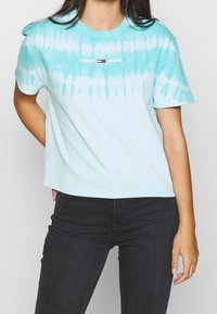 Světle modré tričko s efektom tie-dye, krátké rukávy, zkrácený střih, se znakem "TOMMY JEANS" v červené a černé barvě na hrudi.